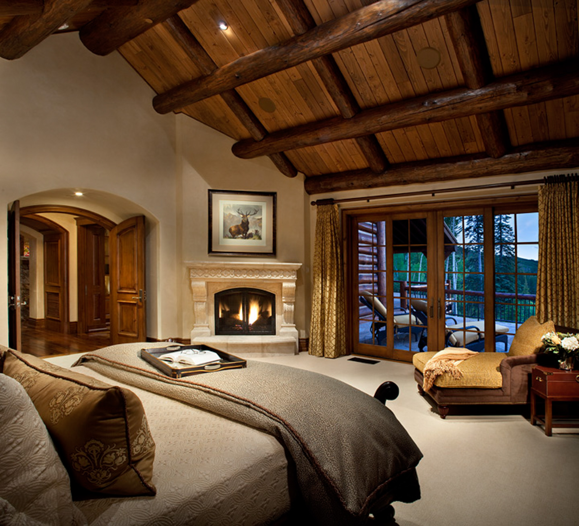 a large bedroom with a rustic log cathedral ceiling and wood burning fireplace at bachelor gulch